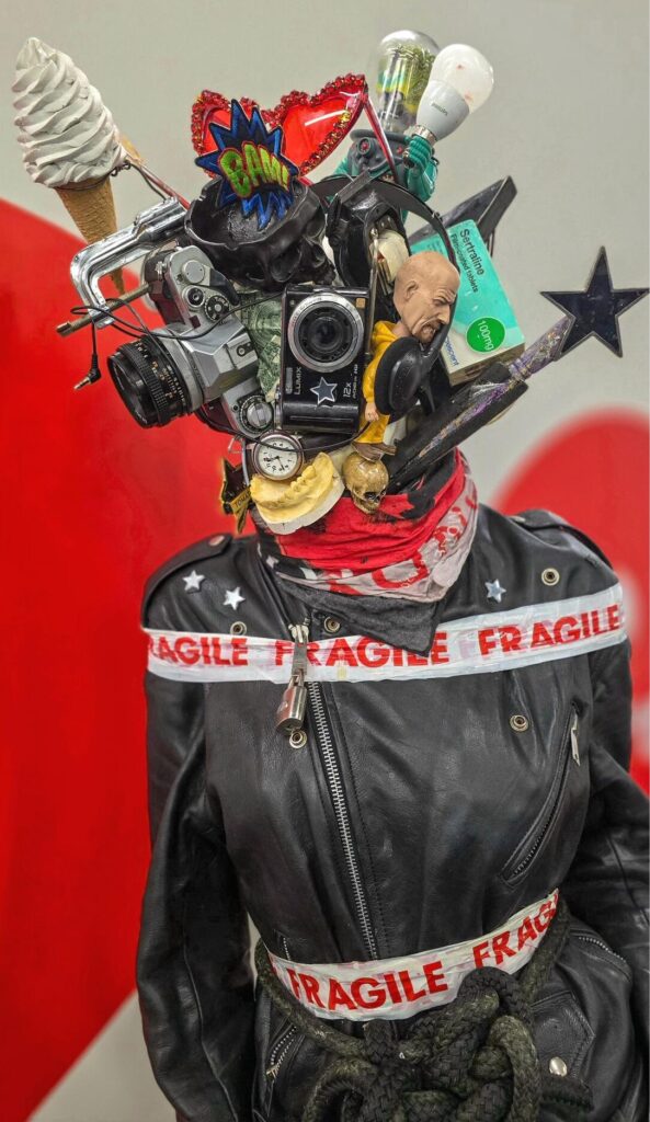 An image showing a art piece made by Michael Forbes named "A Busy Mind" this is to show off the artists own mental health journey. The Mannequin is covered in cameras and everyday household objects. 